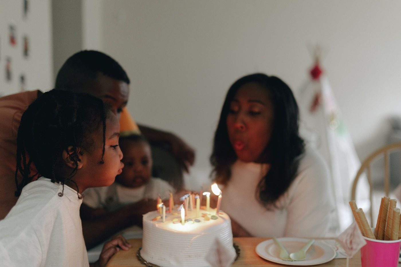 A family gathered around a lit birthday cake as a child blows out the candles